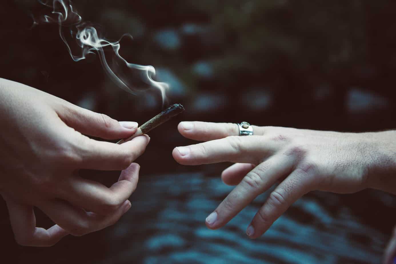 person handing a marijuana joint to friend
