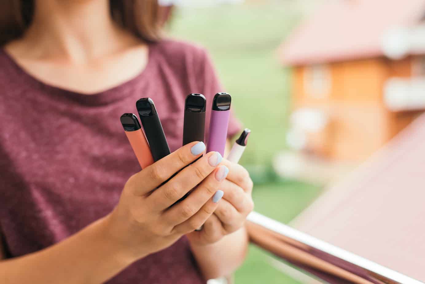 Woman's hands holding various types of disposable e-cigarettes.