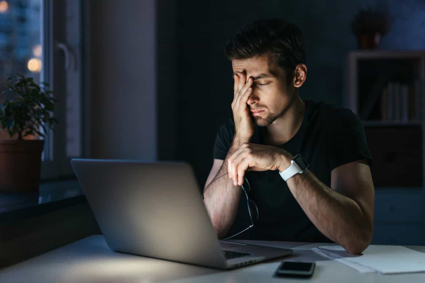 tired and stressed man sits in front of computer in dimly lit room