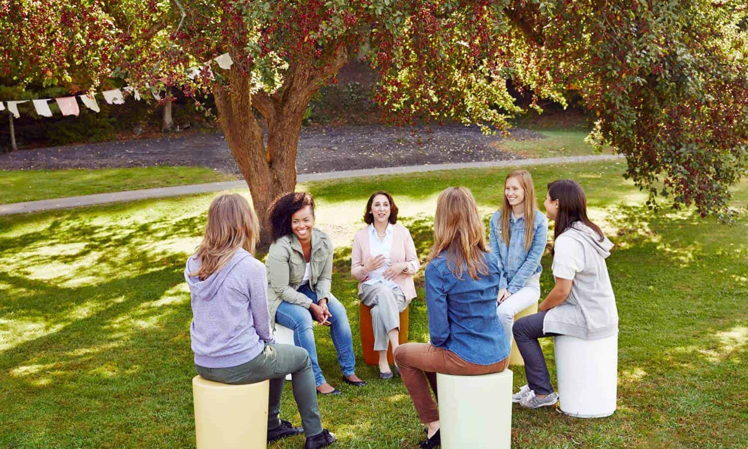 A group of women meeting and talking happily under a tree during a group therapy session at Mountainside