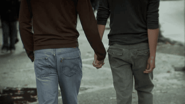 Two men in jeans holding hands by ocean