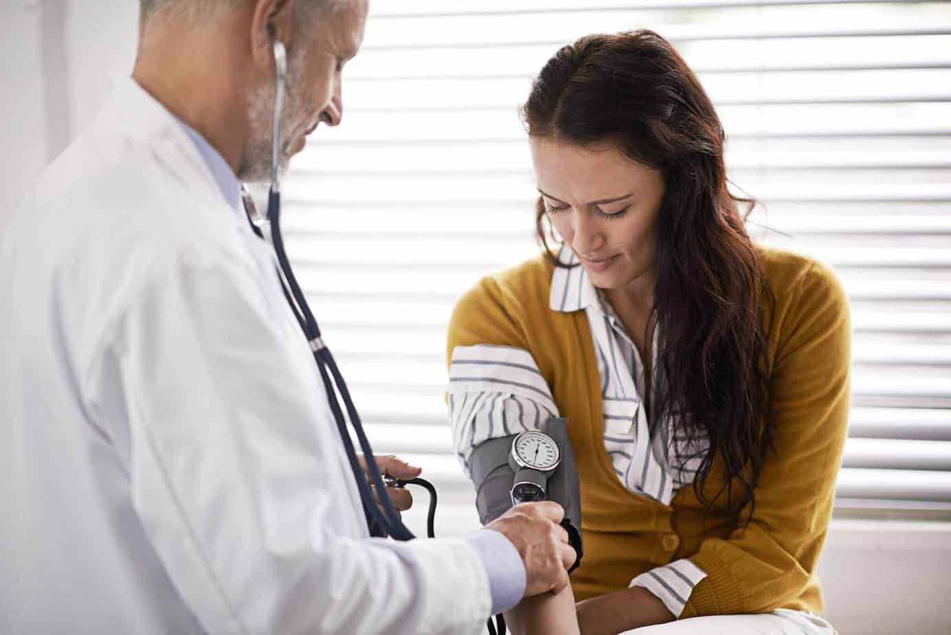 Older male doctor checking a female patient's blood pressure.
