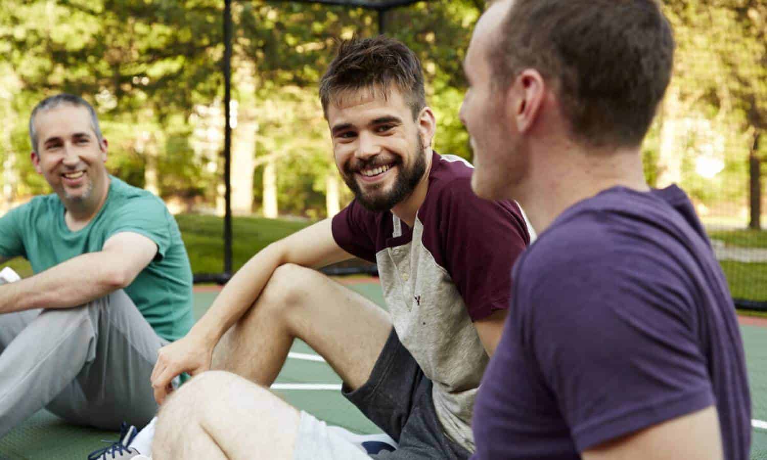 Three men laughing sitting by Basketball Court in Mountainside Treatment Center in Canaan