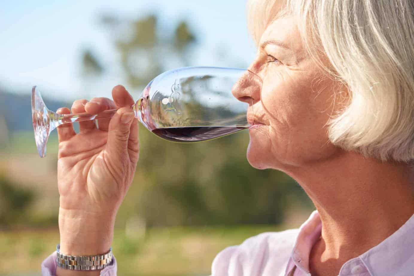 close up of older woman drinking red wine outside