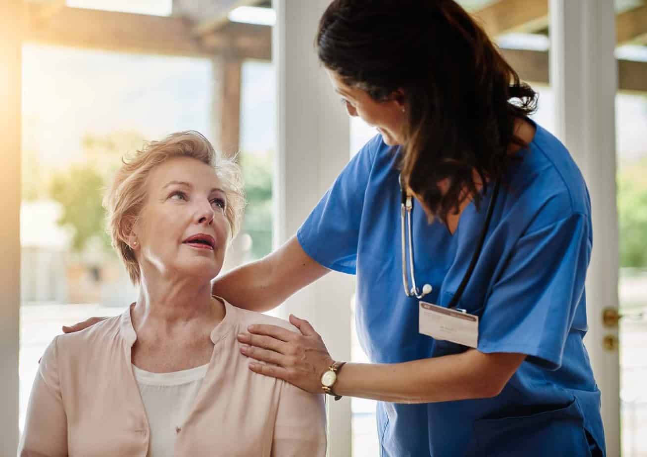 nurse in blue scrubs helping older woman while sitting