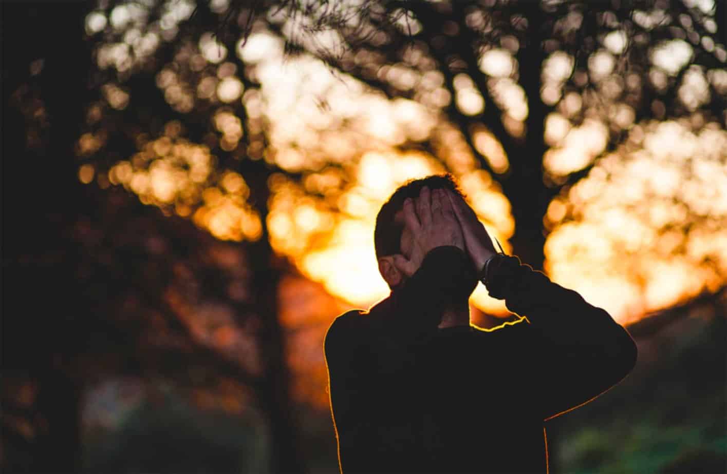 Frustrated man with hands on his face in woods during sunset