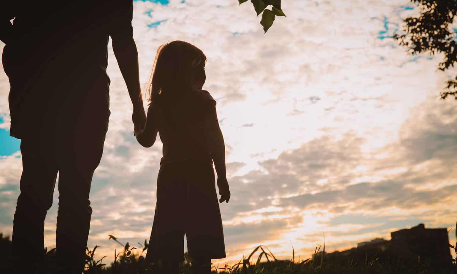 shadow of parent holding hands of female child outside watching sunset