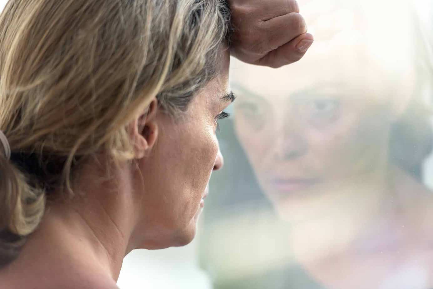 sad woman looking outside window with reflection