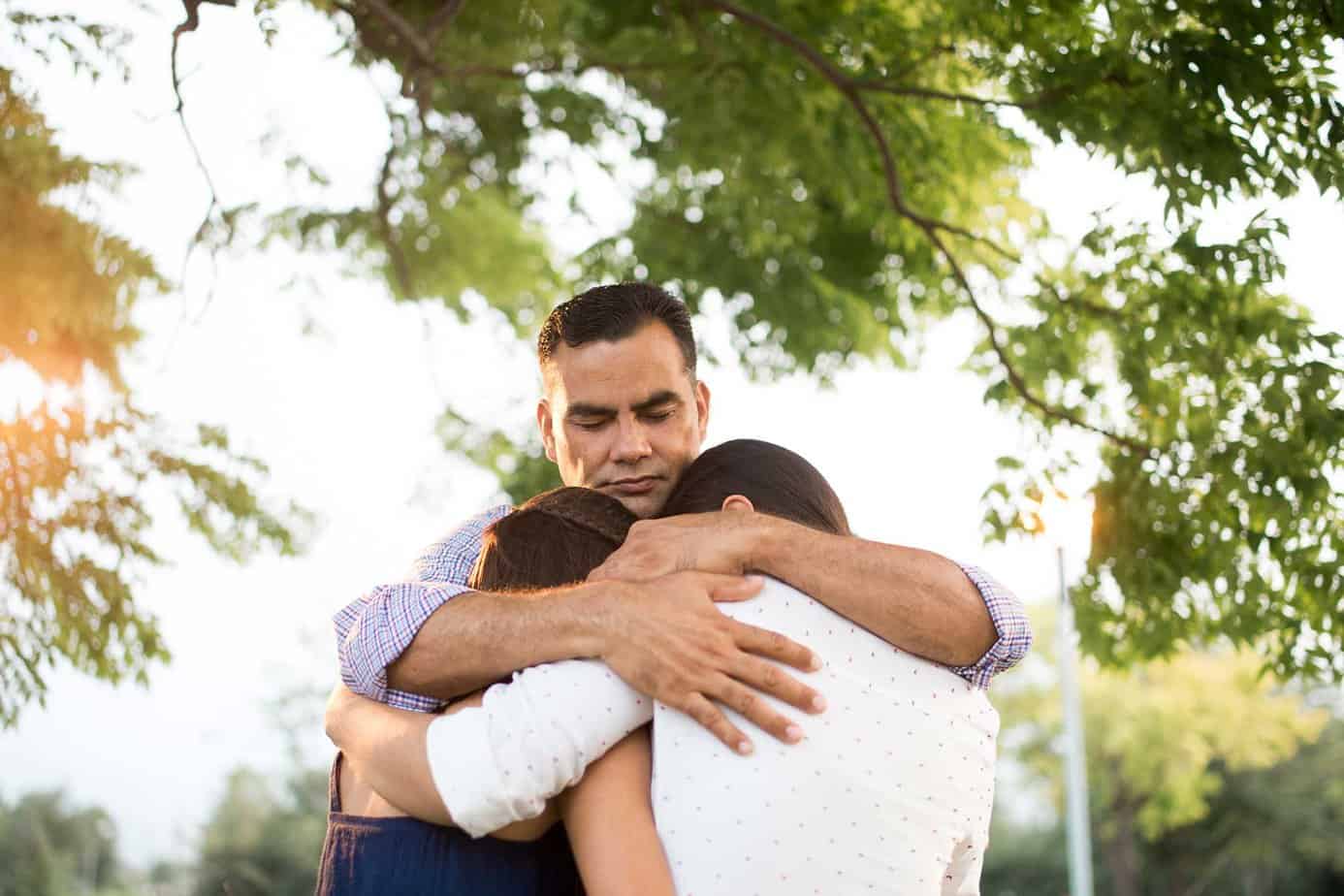 sad man hugging two children outside after surviving a natural disaster