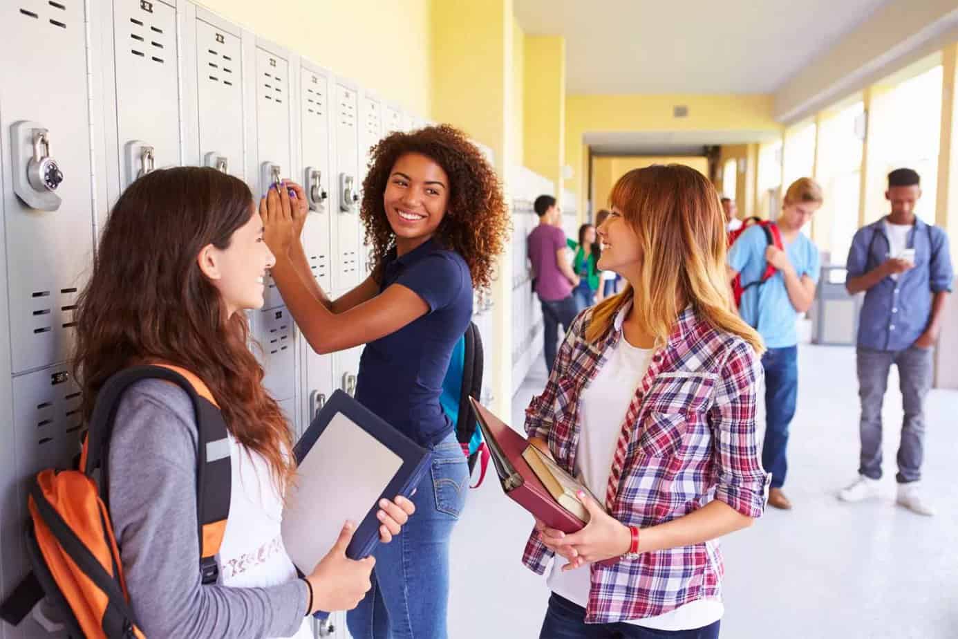 three teenage girls talking and smiling by lockers between classes at high school