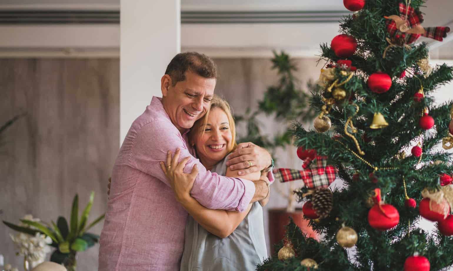 man and woman hugging each other by christmas tree during the holiday season