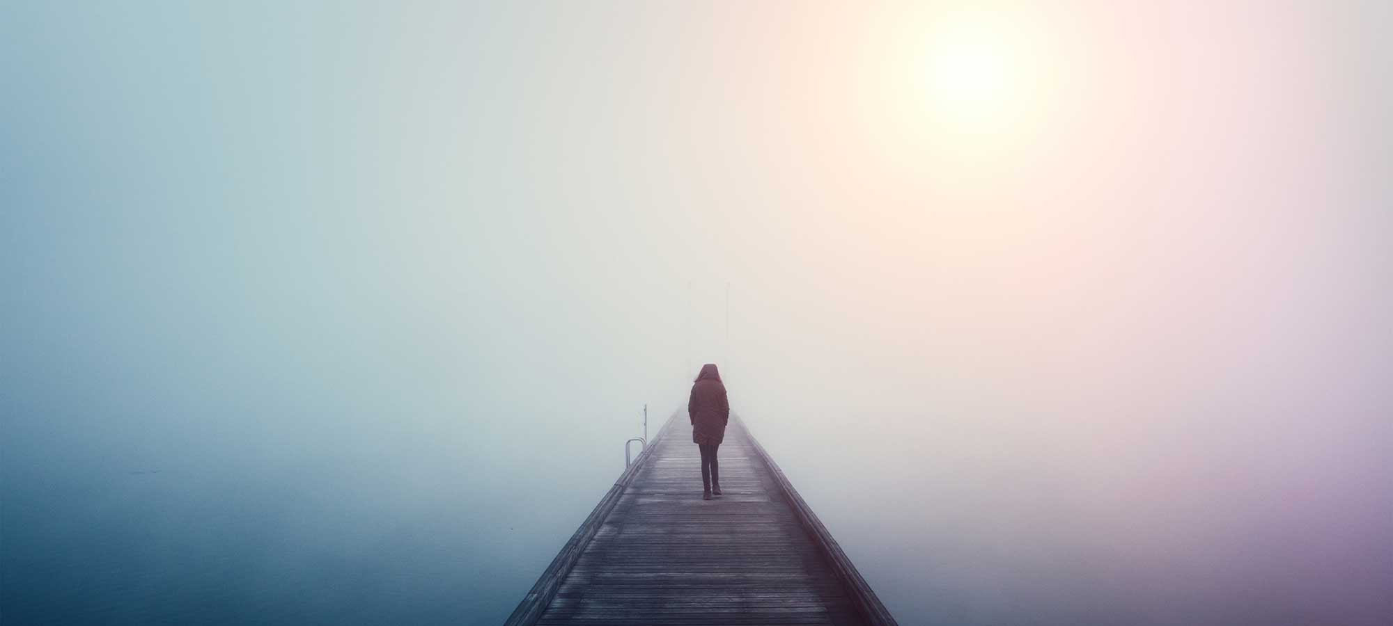 woman in coat walking on pier with fog