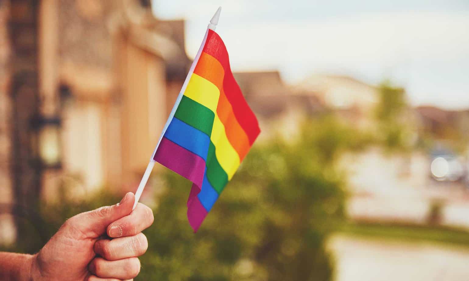 close up of a man holding a LGTBQ+ pride flag outside