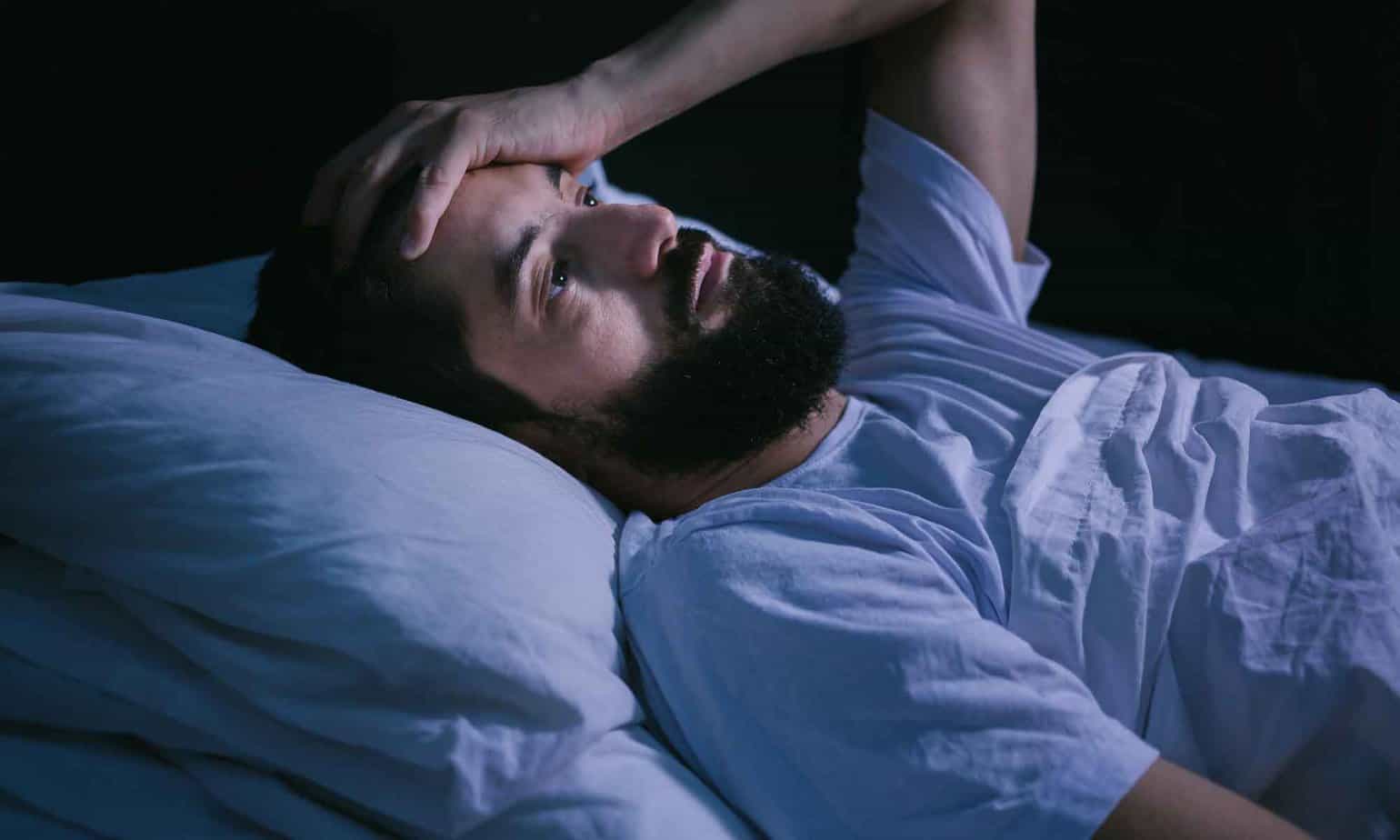 man lying awake in bed after dreaming about relapsing