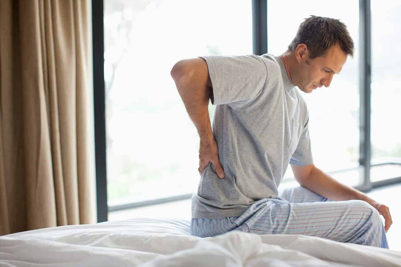 man sitting up in bed near window with lower back pain