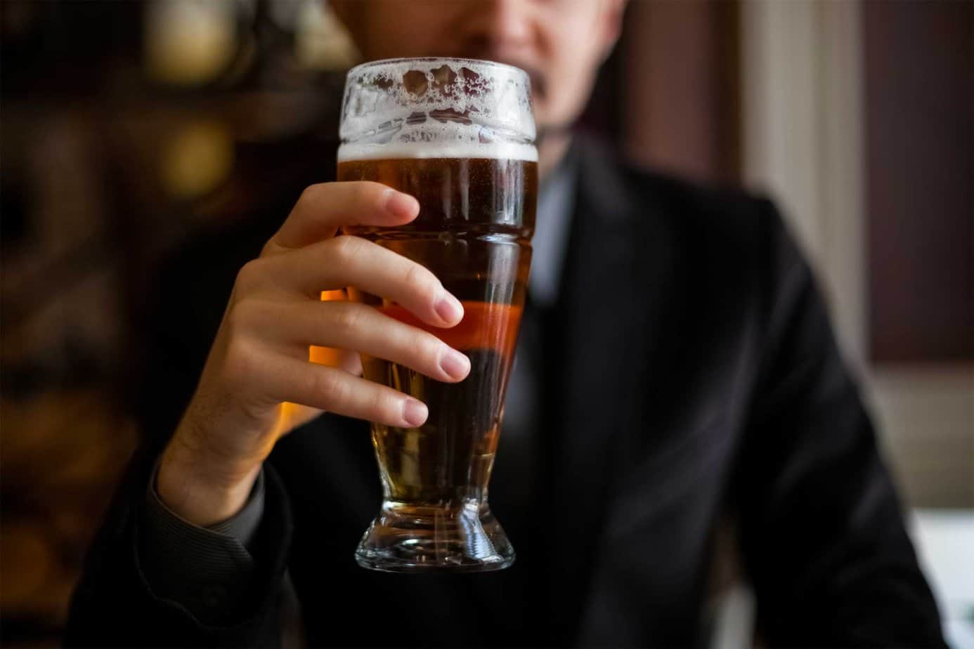 close up of man in suit holding dark ale beer in hand