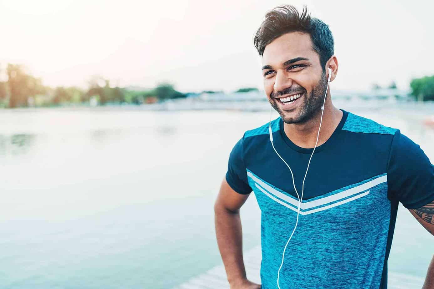 man in blue t-shirt running with headphones smiling by lake