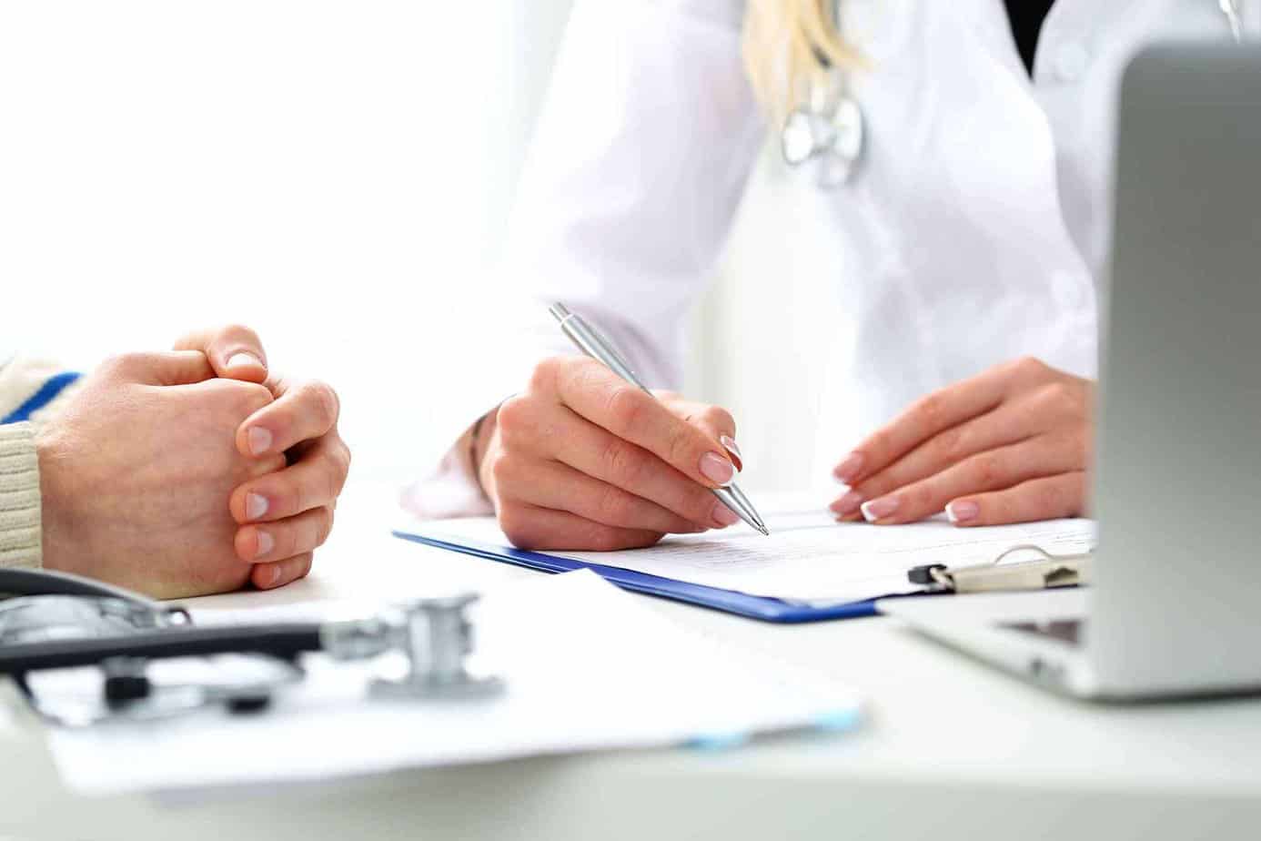 The hands of a doctor and patient reviewing medical paperwork and discussing medication assisted treatment