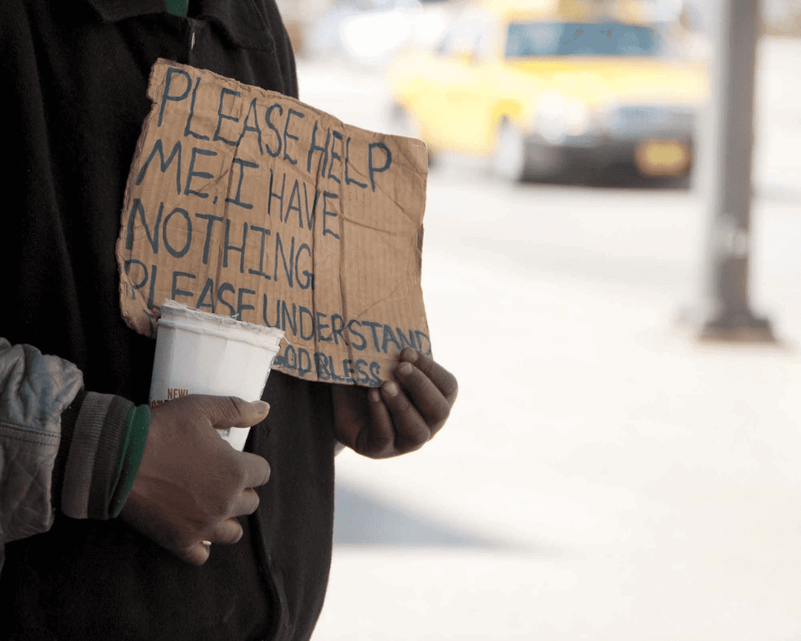 homeless person panhandling in street holding sign that says 