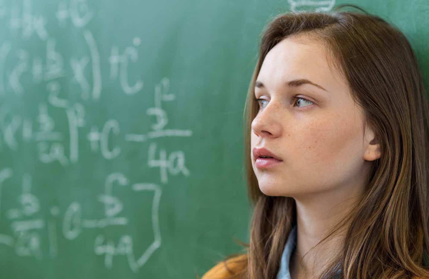 High school female student looking at chalkboard with math