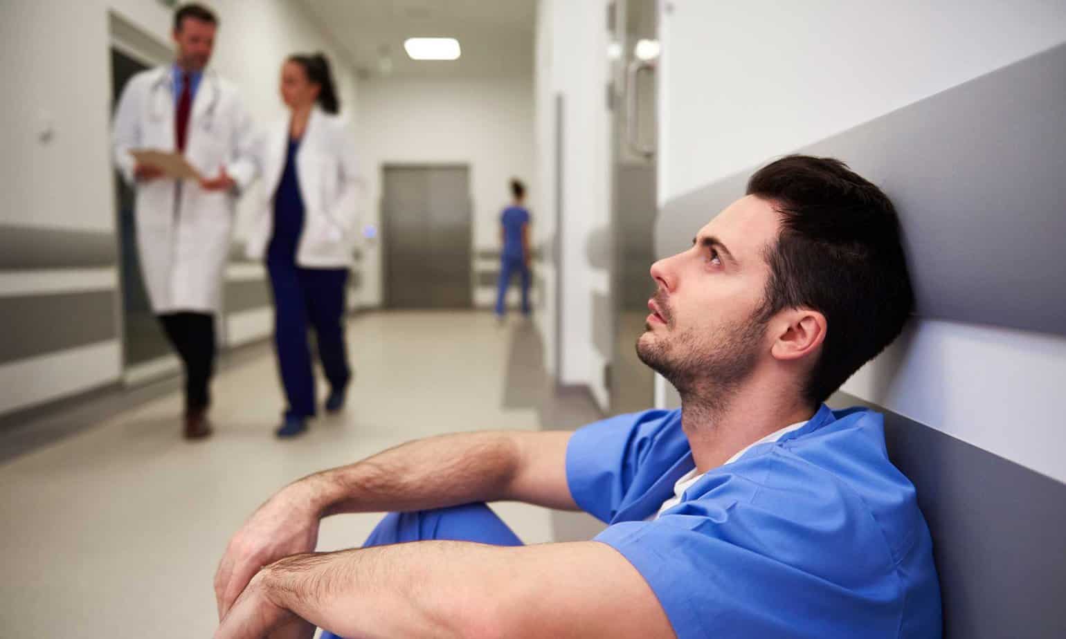 A stressed out doctor sitting on the ground in a hospital hallway.