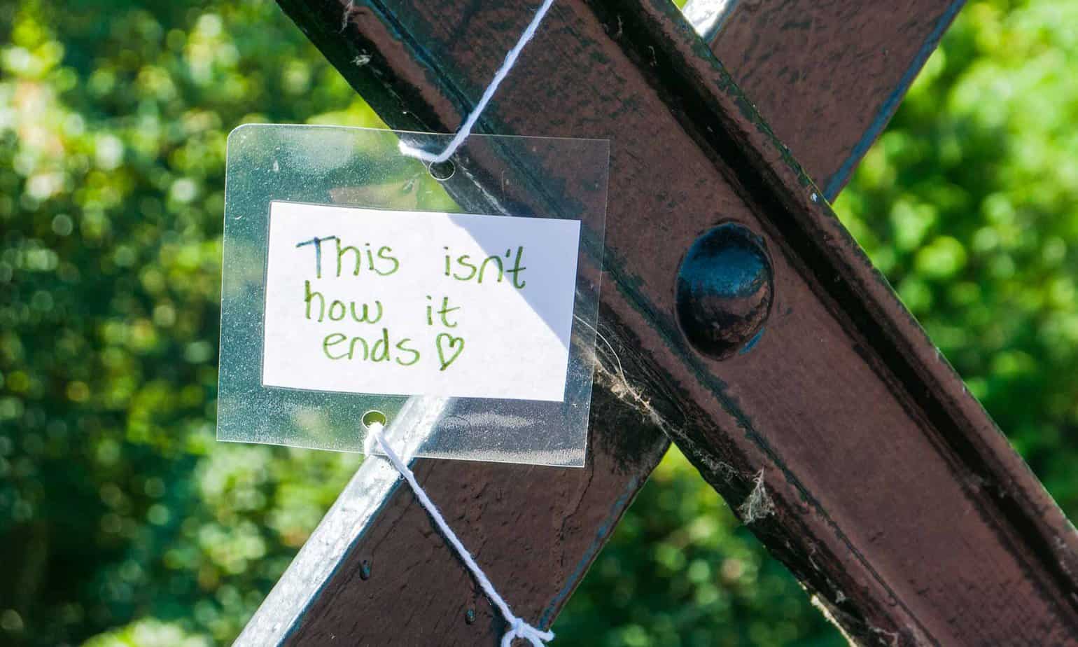 suicide prevention note that says, " This isn't how it ends" hanging on a bridge