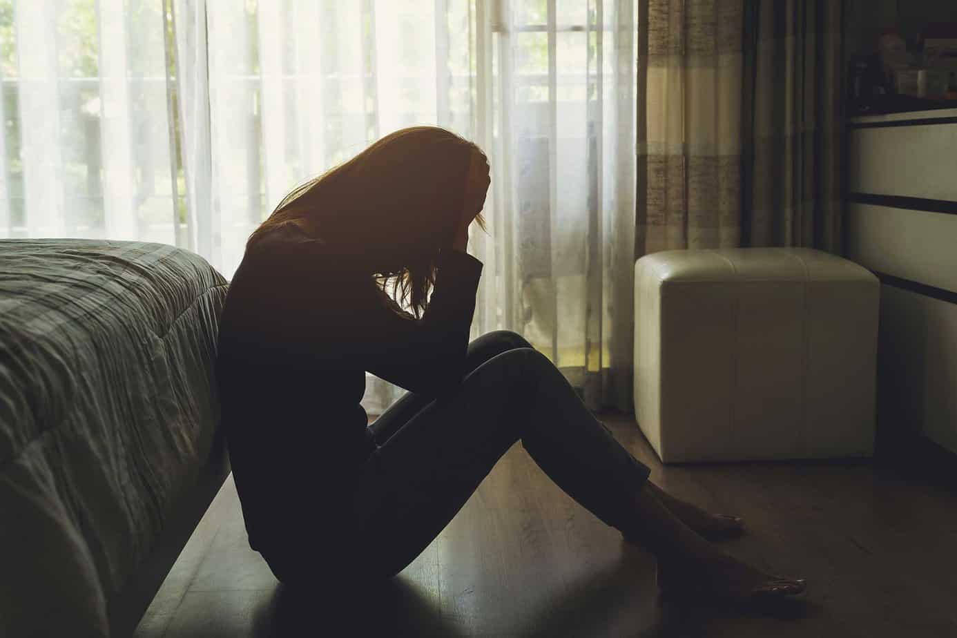 depressed silhouette of woman sitting on ground in dark room