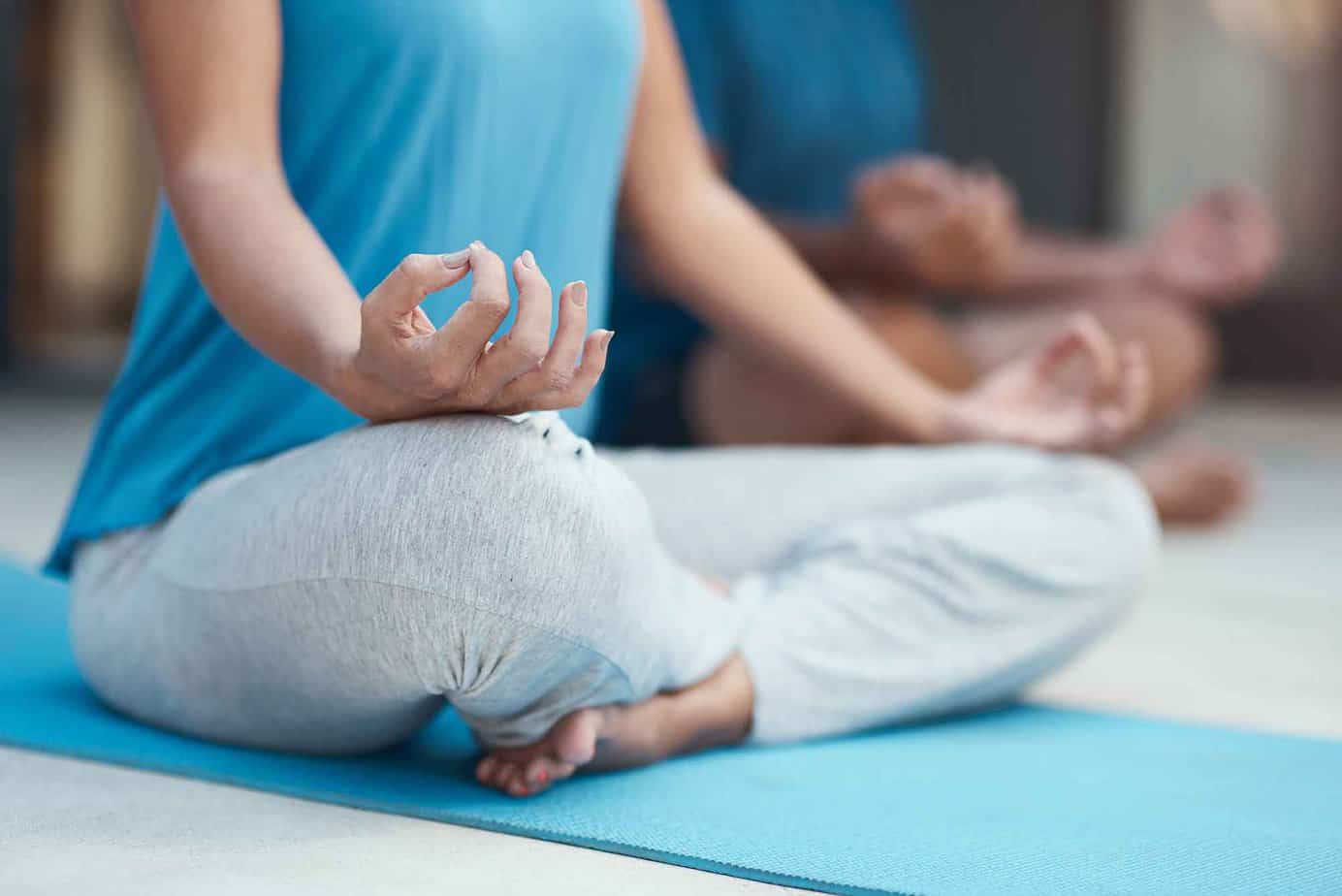 A woman in a blue shirt with gray sweatpants meditating in a drug rehab yoga class.