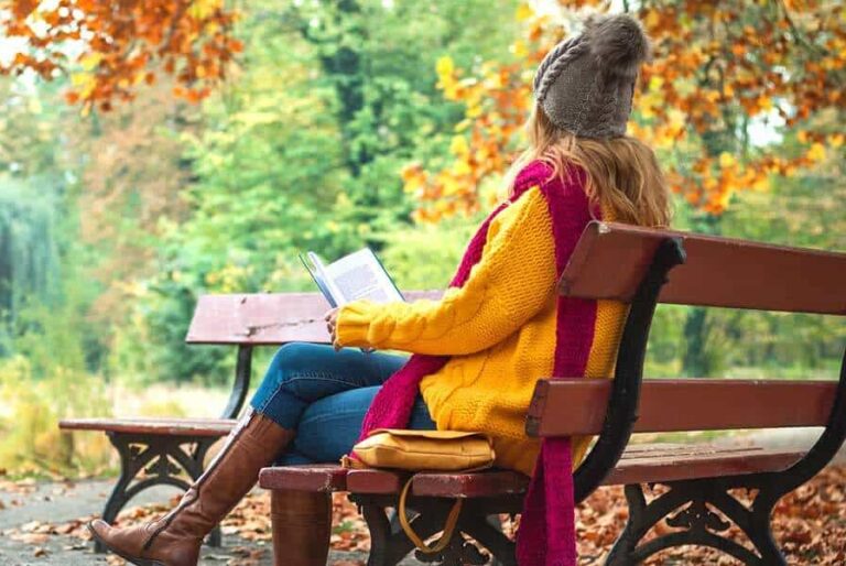 woman sitting on bench outside in Fall reading a book