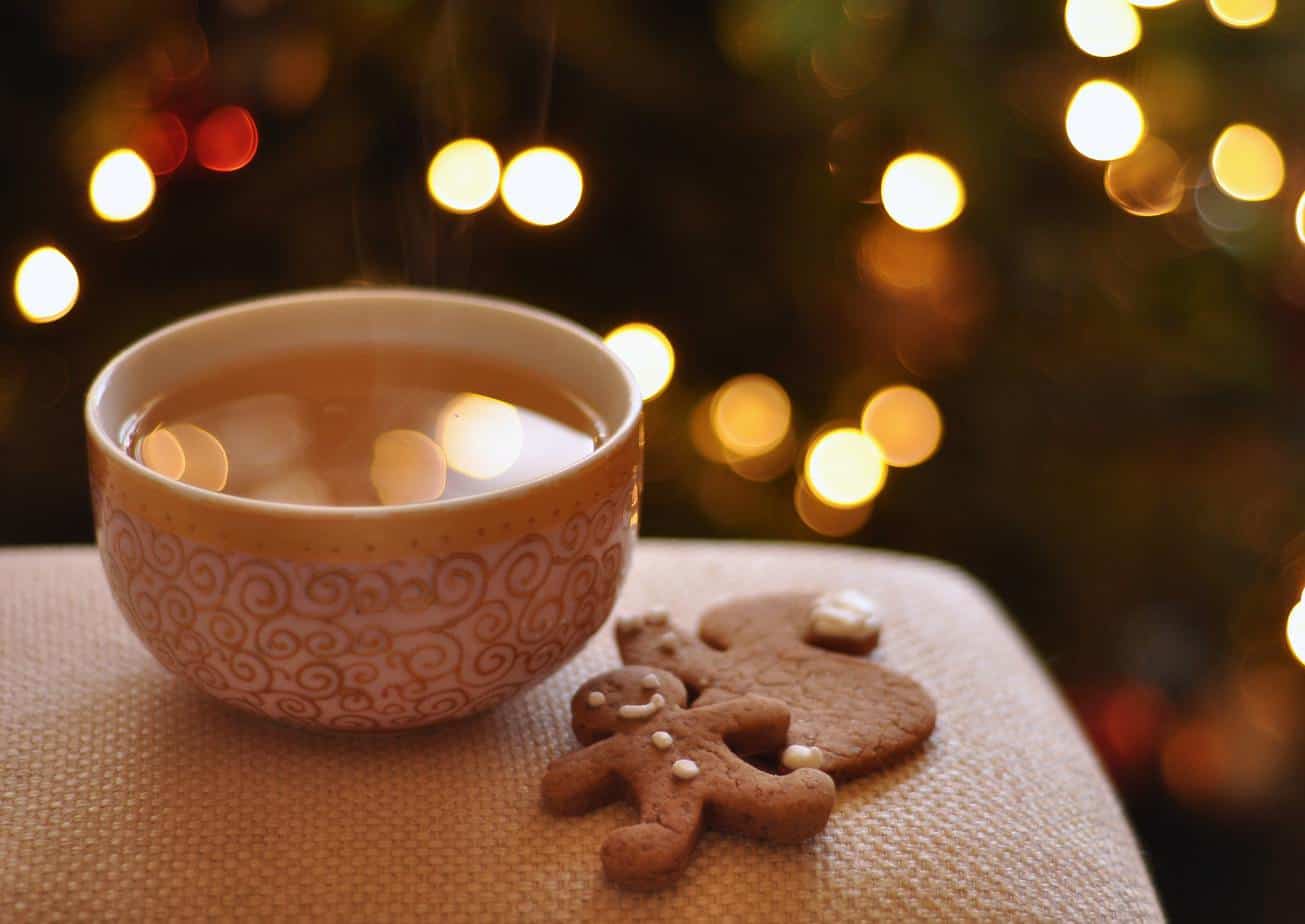 gingerbread men next to warm cup of tea by christmas decorations