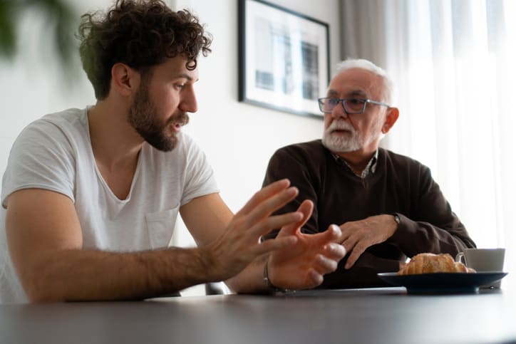 Worried man discussing boundaries in recovery with his son while seated at kitchen table