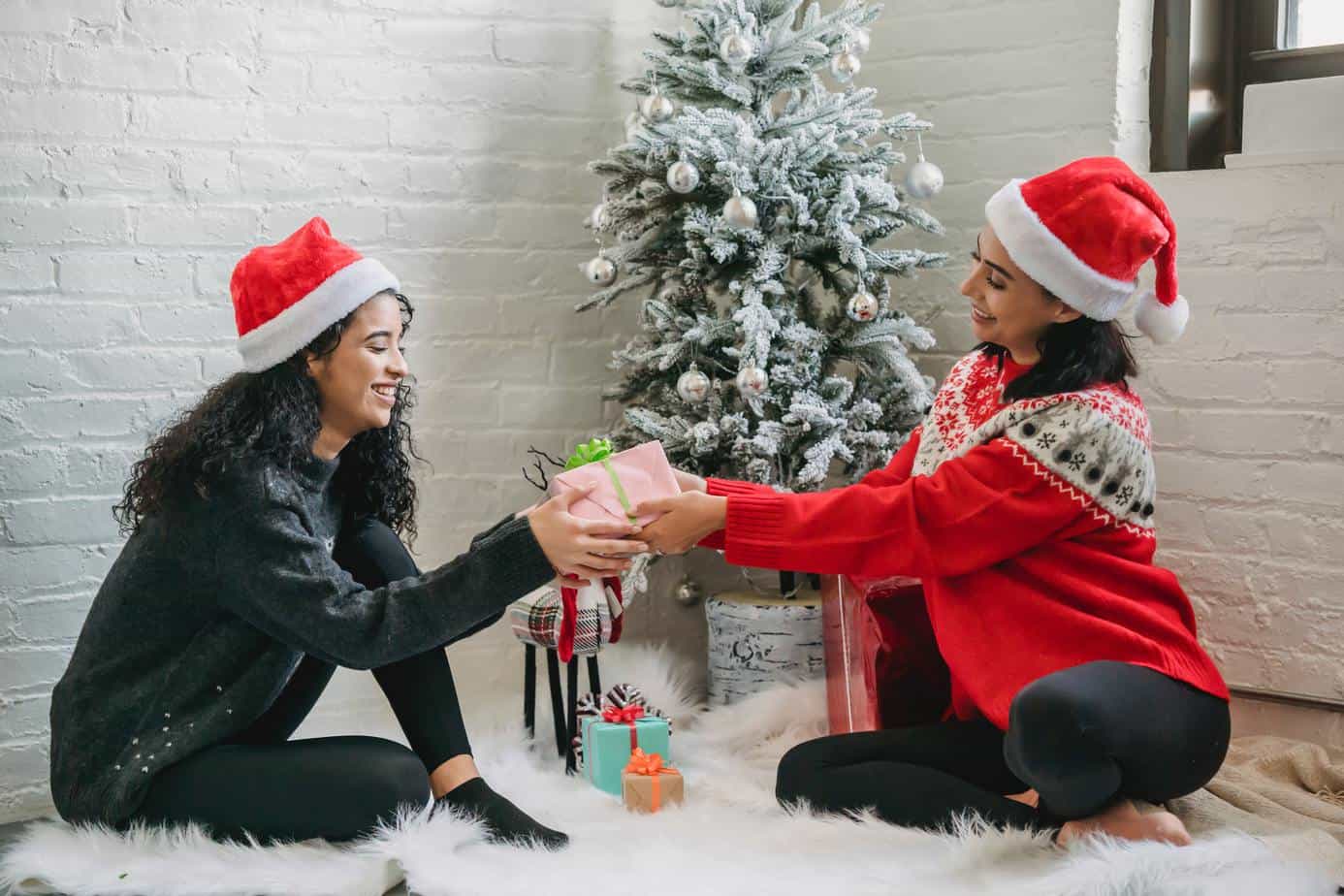 two women exchanging holiday gifts next to Christmas tree