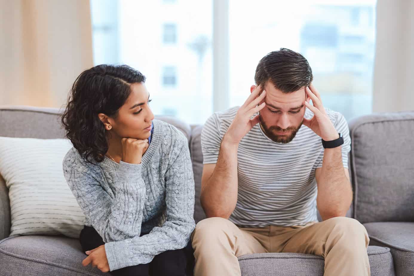 man and woman seated on couch in living have difficult conversation; man experiences triggers