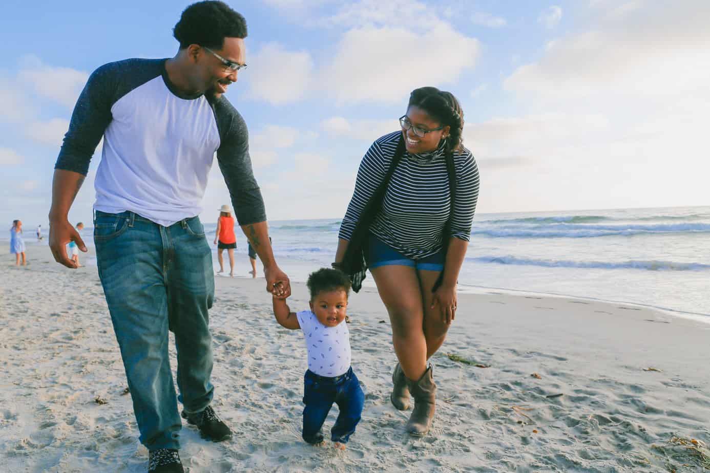 A family of three explores a beach; mom and dad hold onto the hands of their child