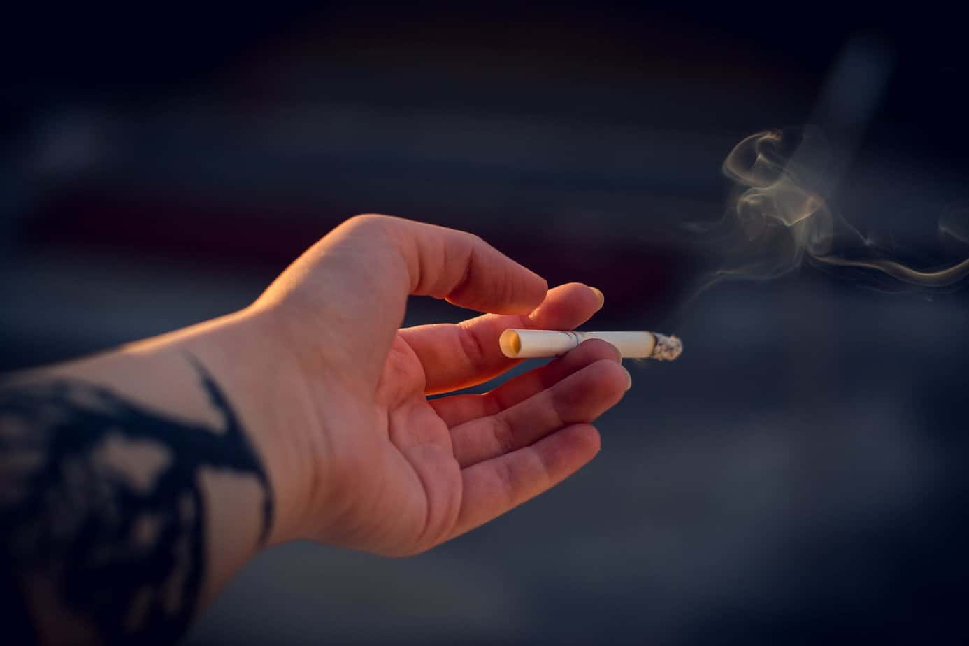 A person holds out a lit cigarette, smoking it