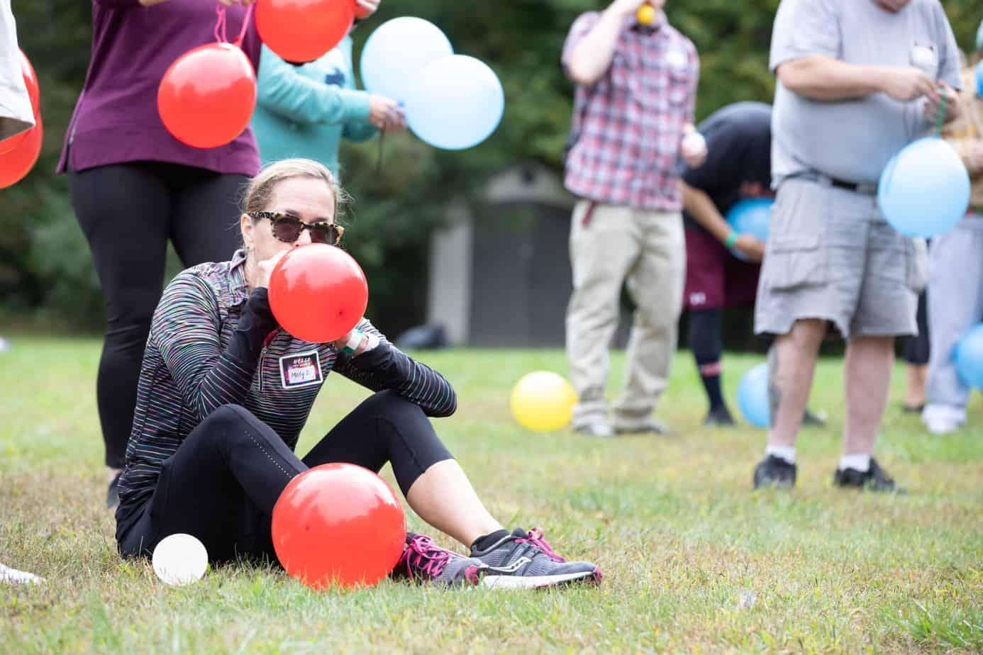 A woman blowing up a red balloon on the lawn at Mountainside addiction treatment center