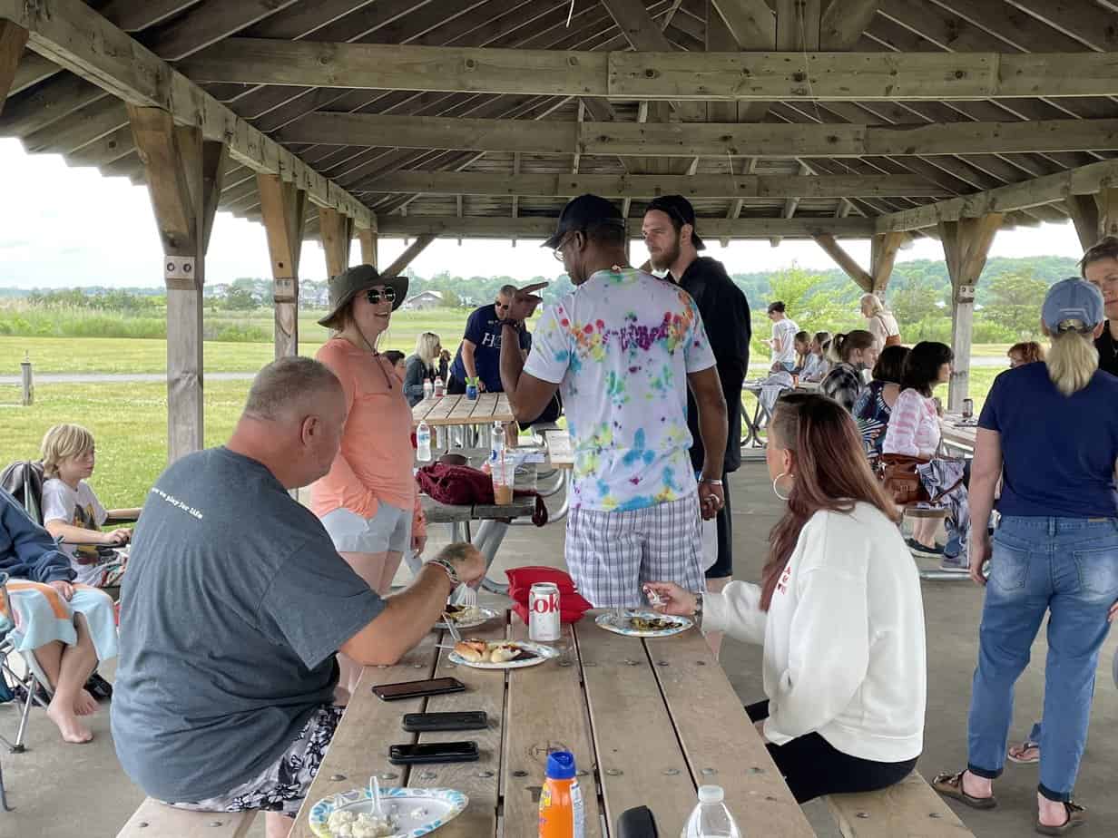 Alumni talking and eating around picnic table at Mountainside Treatment Center Alumni Sober Beach BBQ 2022