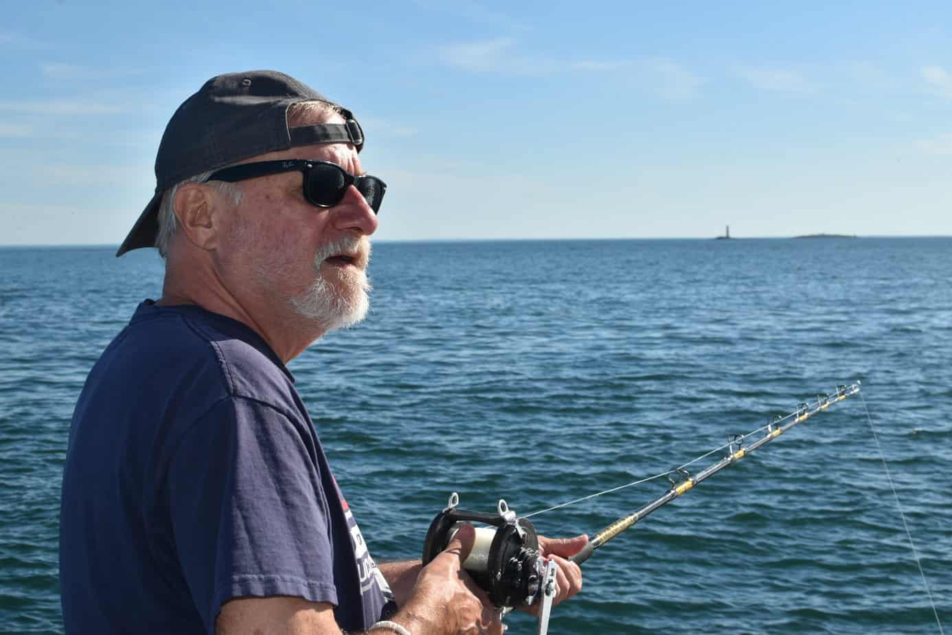 Older man in sunglasses and hat holding fishing road by ocean at Mountainside Treatment Center Extended Care Fishing Event September 2022