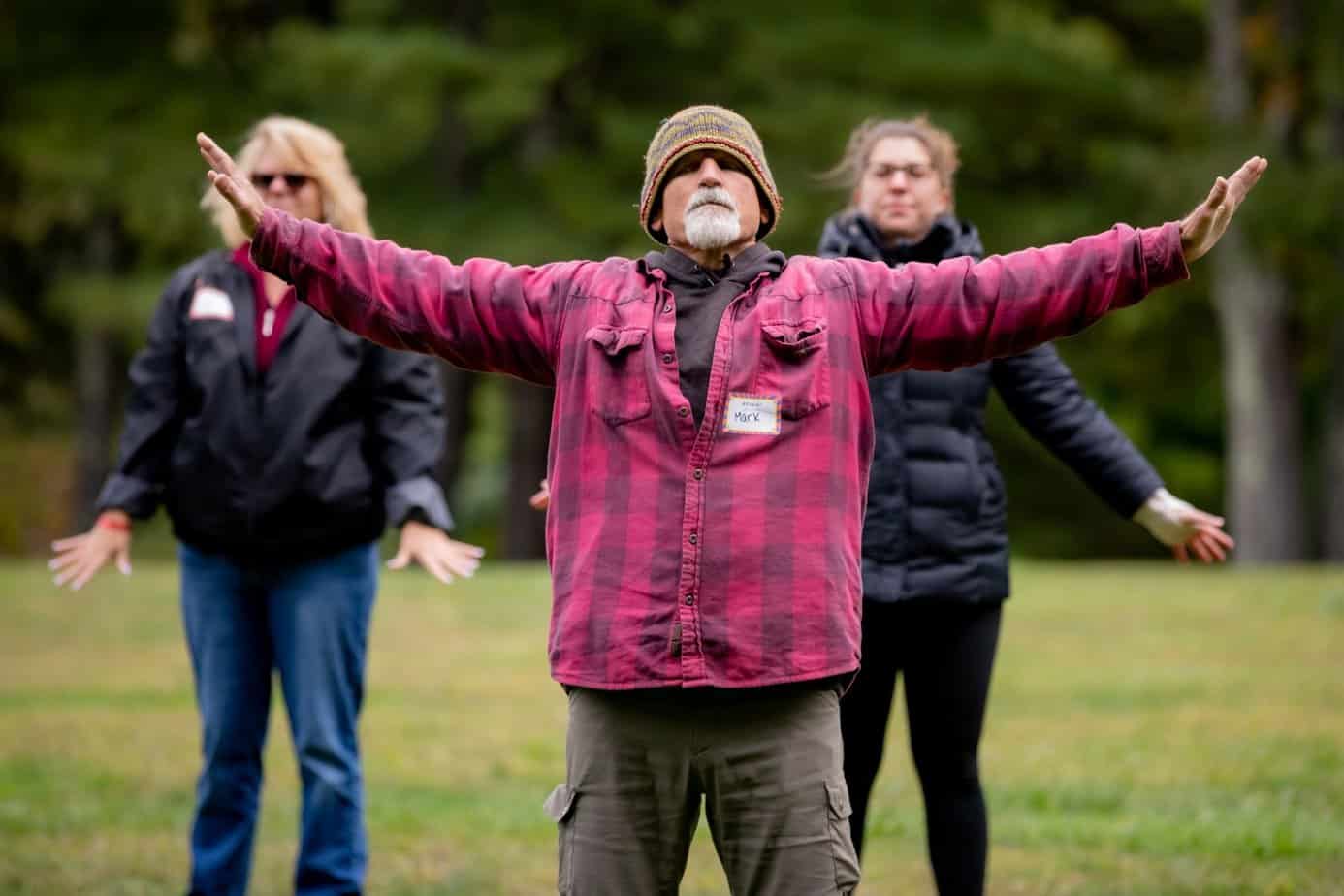 Older man in hat and red coat leading yoga class outside