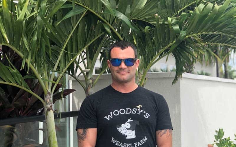 man in sunglasses smiles in front of tropical tree