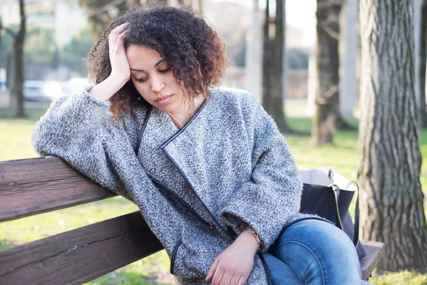 sad woman in coat seated on bench with head in hands