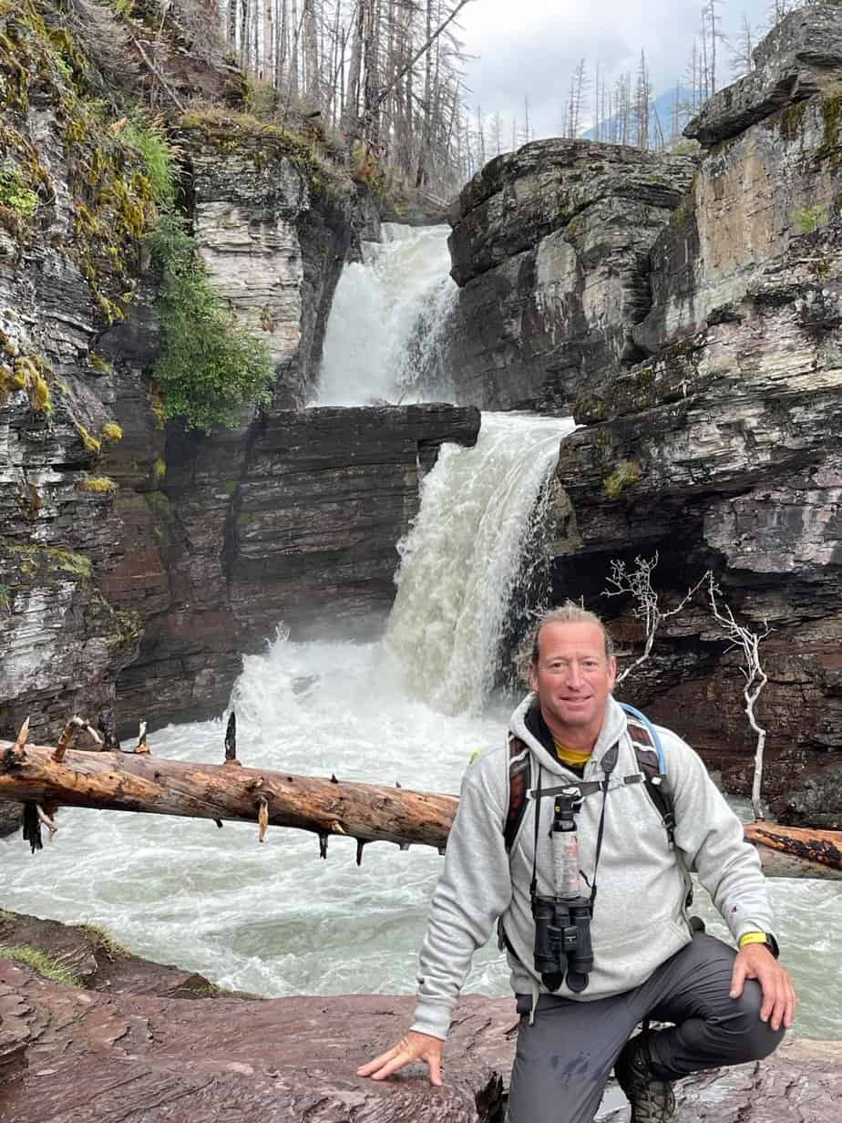 man poses in front of waterfall in forest