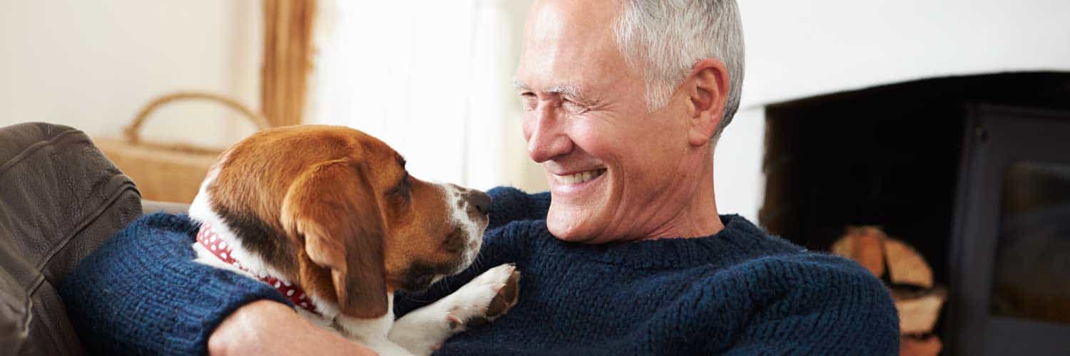 smiling man sitting on couch with dog resting on his chest