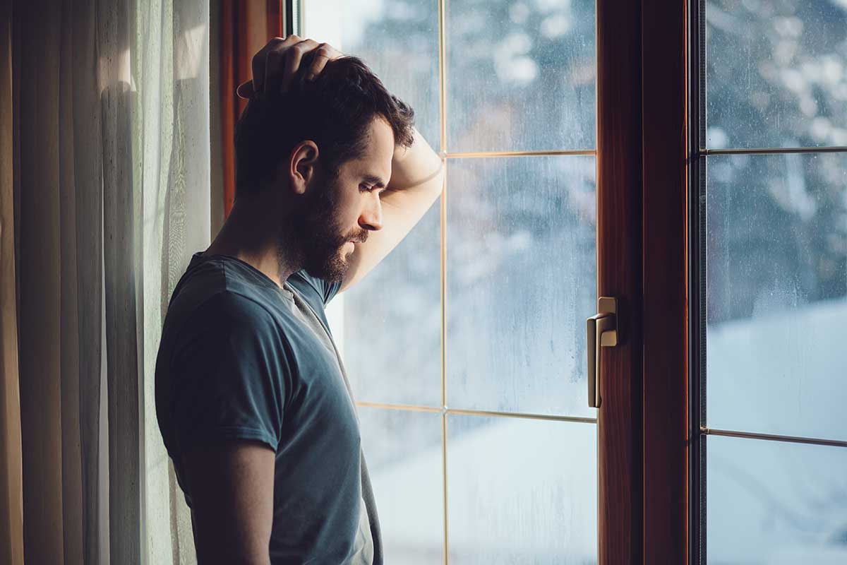 sad man gazing out of window in dark room