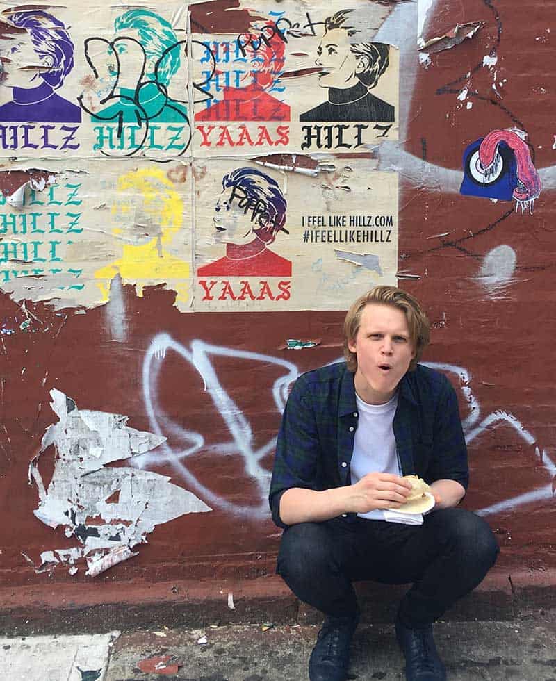 man eating sandwich in front of graffiti wall