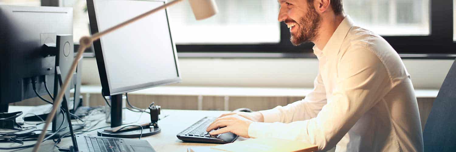 smiling man sitting at desk typing on computer