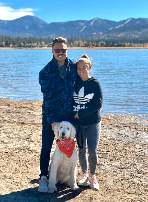 woman and man stand by lake together with dog