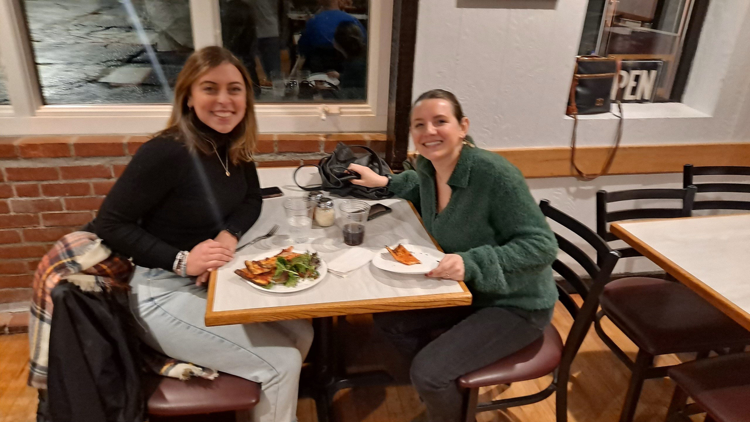 Two women smiling around table with food at Mountainside Treatment Center Alumni Pepe's Pizza Event in Connecticut 2023