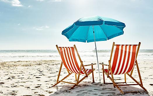 Two striped beach chairs and a blue umbrella on a sunny beach.