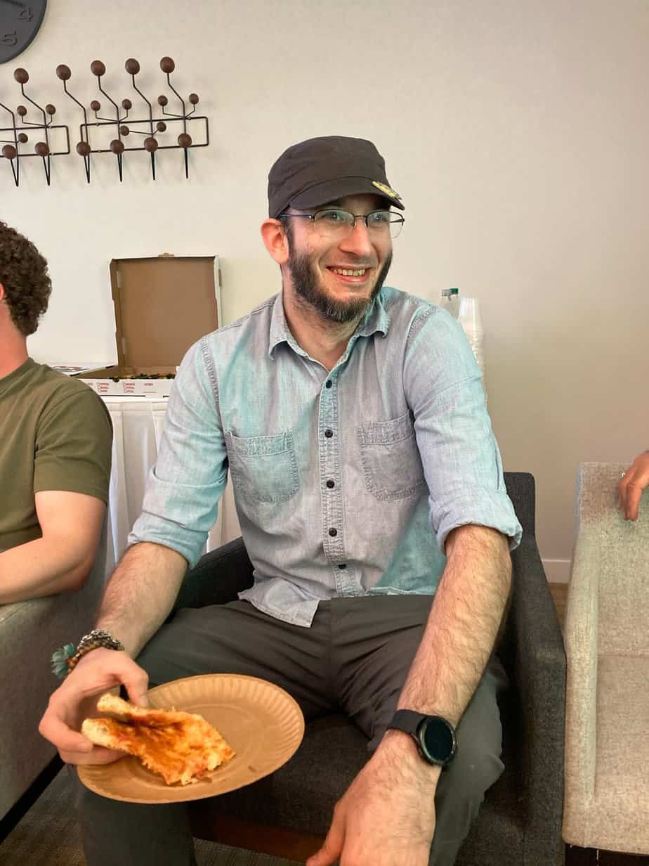 Man smiling eating pizza at Alumni 2023 Pizza Social at Mountainside Canaan